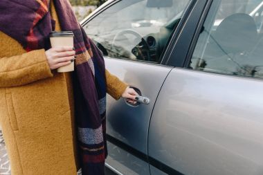 partial view of woman with coffee to go in hand holding car door handle clipart