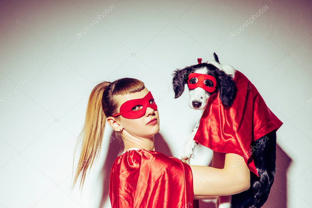 side view of young woman and puppy in superhero costumes
