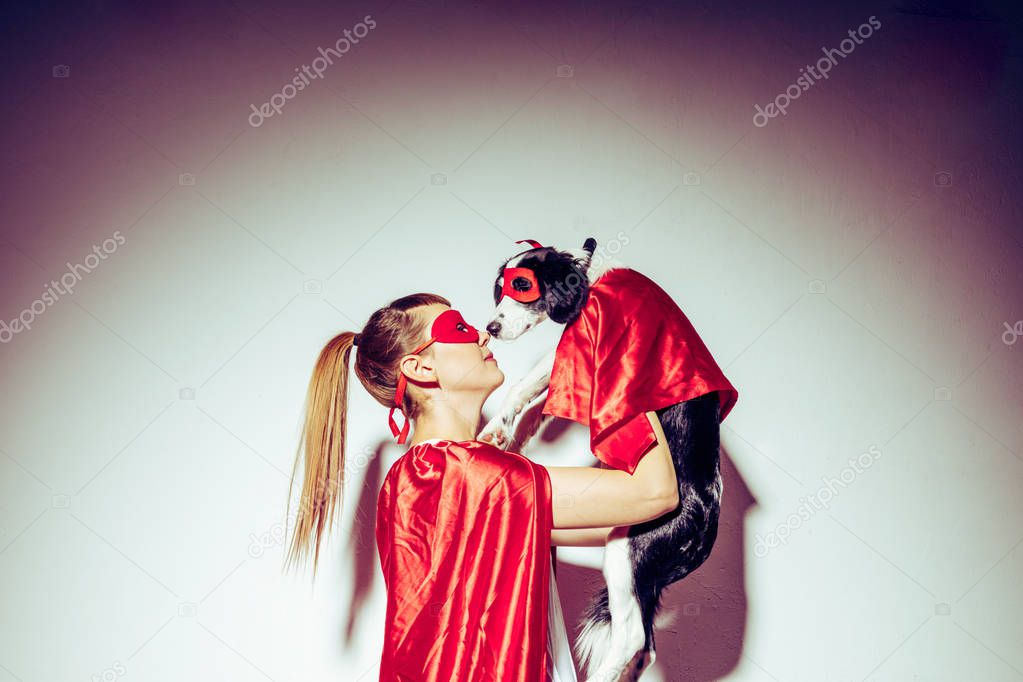 side view of young woman and little puppy in red masks and capes