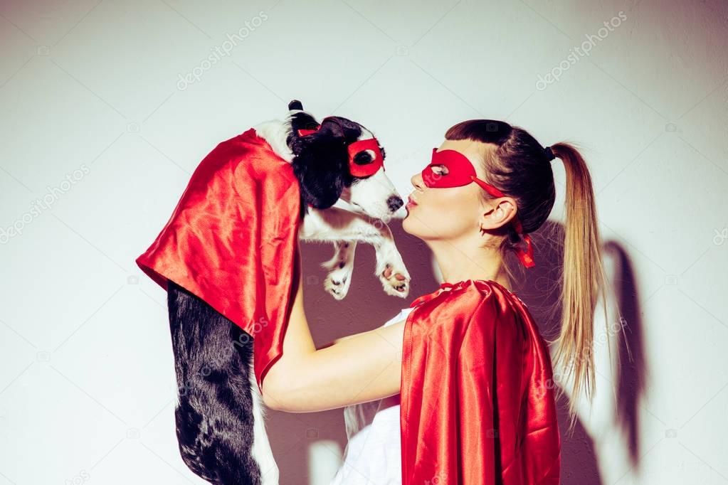 side view of woman kissing puppy in superhero costume