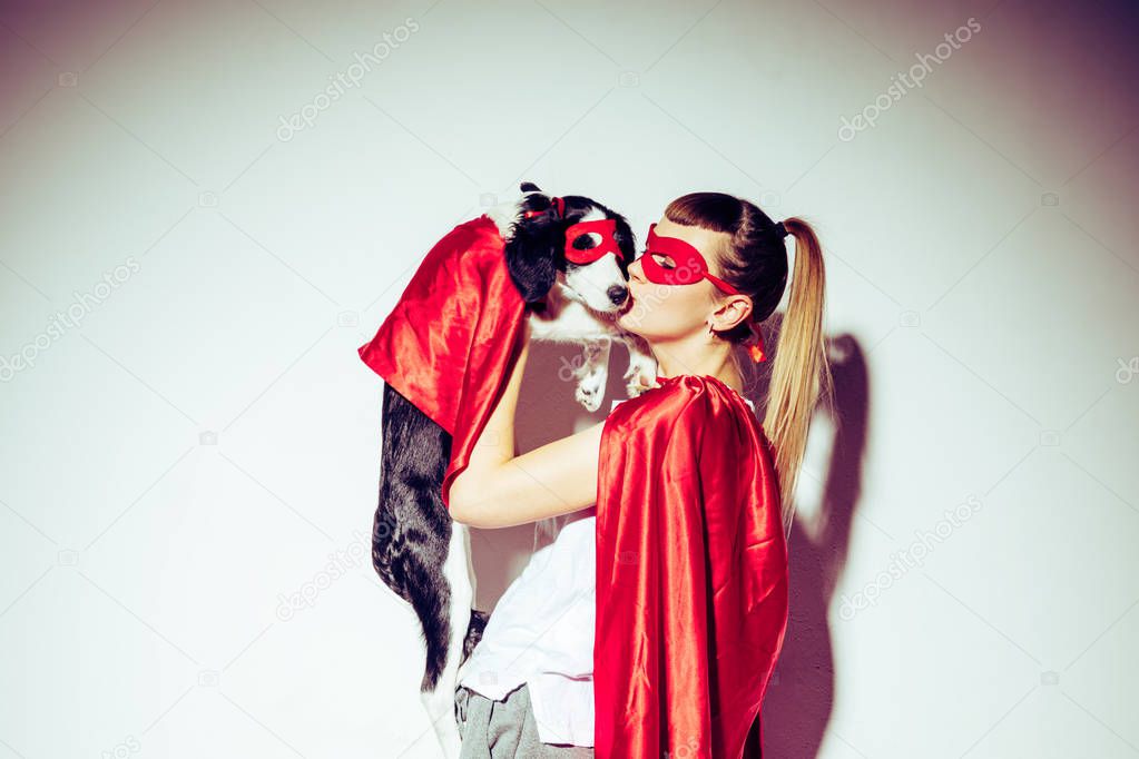 side view of woman kissing puppy in superhero costume