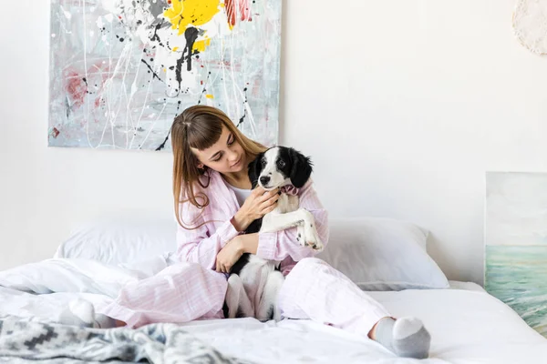 Porträt einer hübschen Frau im Pyjama, die kleine Welpen hält, während sie zu Hause im Bett liegt — Stockfoto