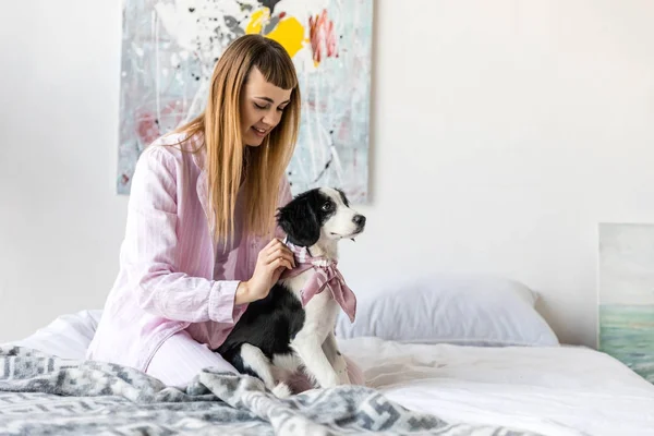 Lächelnde Frau im Schlafanzug und niedlicher kleiner Welpe, der morgens zu Hause auf dem Bett liegt — Stockfoto