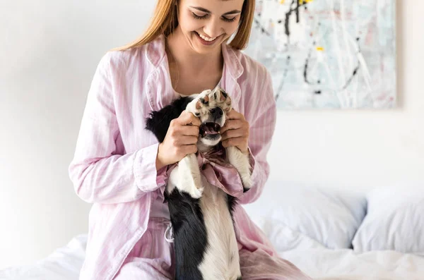 Glückliche Frau im Pyjama und süßer kleiner Welpe, der morgens zu Hause Spaß hat — Stockfoto