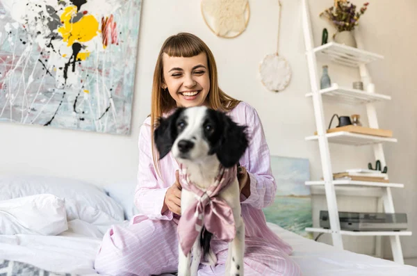 Foco seletivo de mulher sorridente em pijama e filhote de cachorro adorável na cama em casa — Fotografia de Stock