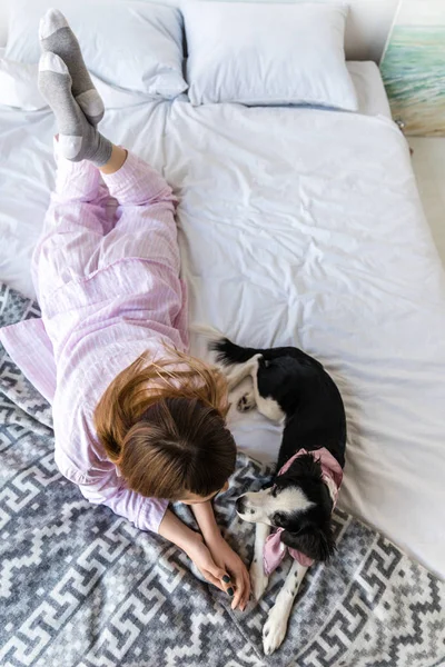 Overhead view of woman in pajamas lying on bed together with cute puppy — Stock Photo