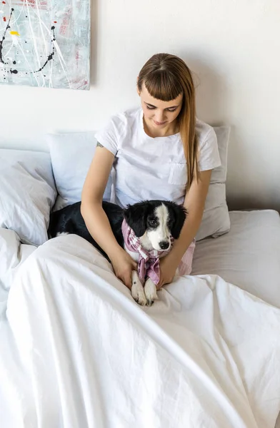 Portrait of young woman and cute puppy lying together in bed in morning at home — Stock Photo