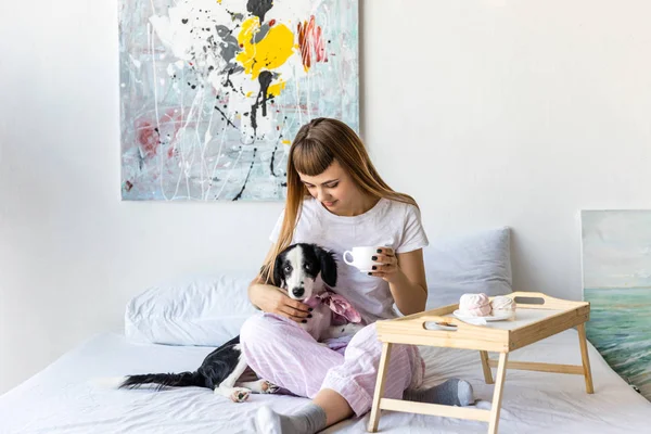 Mulher beber café enquanto descansa na cama junto com filhote de cachorro — Fotografia de Stock