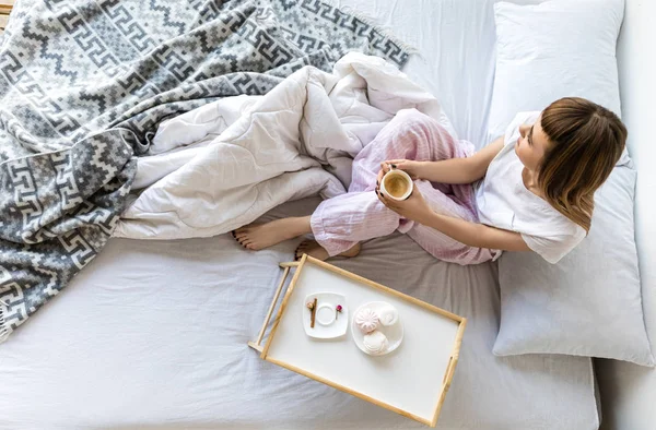 Blick von oben auf eine Frau mit einer Tasse Kaffee, die morgens auf dem Bett sitzt — Stockfoto