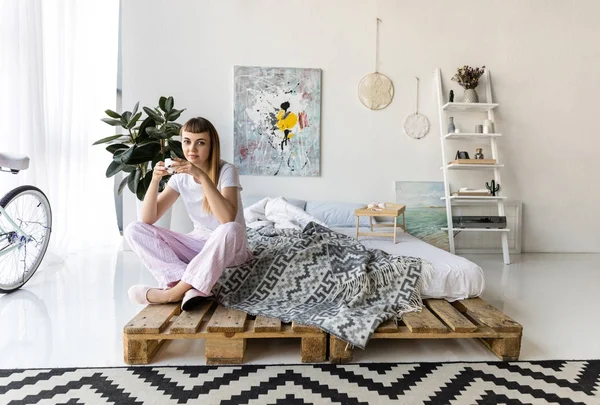 Jeune femme en pyjama avec tasse de café reposant sur le lit le matin — Photo de stock