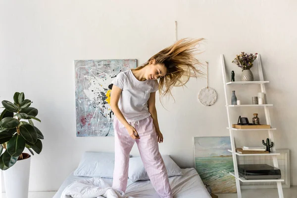 Joyeuse jeune femme en pyjama dansant sur le lit le matin à la maison — Photo de stock