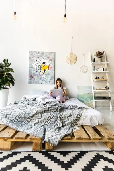 Сфокусированная молодая женщина с помощью ноутбука во время отдыха в постели утром дома — стоковое фото