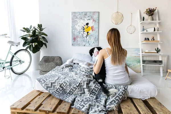 Visão traseira da mulher e filhote de cachorro sentado na cama juntos em casa — Fotografia de Stock