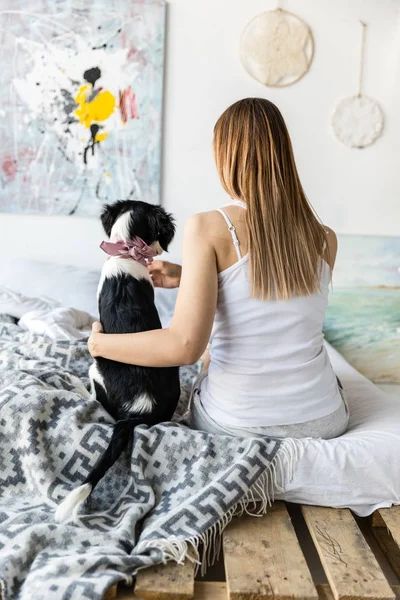 Visão traseira da mulher e filhote de cachorro sentado na cama juntos em casa — Fotografia de Stock