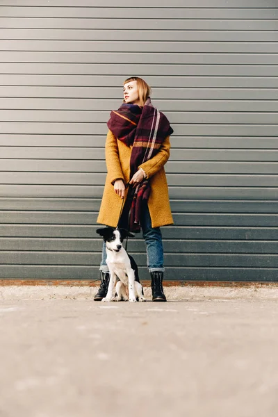 Fashionable woman with puppy on dog lead standing on street — Stock Photo