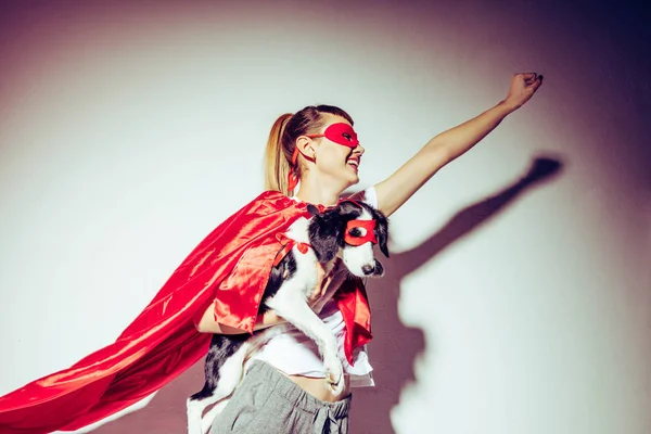 Vue latérale de femme souriante et petit chiot en costumes de super-héros — Photo de stock