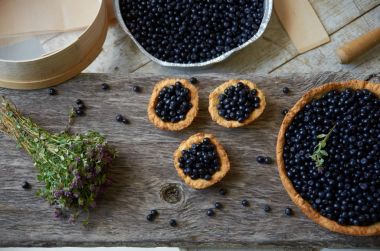 Üç yaban mersinli kek ve gri bir tahta üzerinde çiçekler olan bir pişmiş pasta 