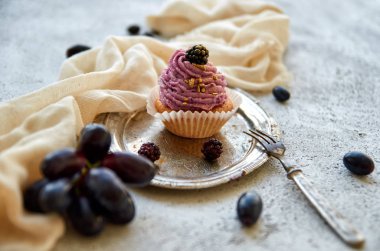 Vintage gümüş tepsi üzerinde blackberry ile mor altın cupcake tatlı çatal, hafif kahverengi kumaş, taze üzüm mavi ve gri beton zemin üzerine böğürtlen dalı ile dekore edilmiştir. Görünümü kapatın