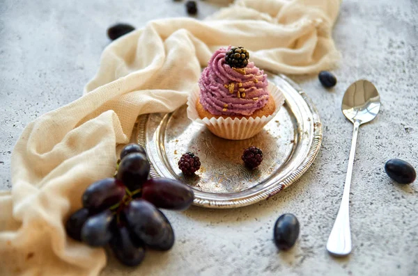Mor altın cupcake uzun kaşıkla, hafif kahverengi kumaş, dekore edilmiş vintage gümüş tepsi üzerinde blackberry ile taze mavi üzüm ve gri beton zemin üzerine böğürtlen dalı yakın çekim