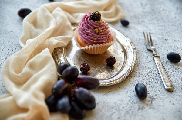 Tatlı çatal, hafif kahverengi kumaş, taze üzüm mavi ve gri beton zemin üzerine böğürtlen dalı ile dekore edilmiş vintage gümüş tepsi üzerinde blackberry ile mor altın cupcake