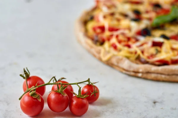 Pizza vegetariana caliente con tomates, pimiento, cebolla, aceitunas negras, queso y especias sobre fondo blanco borroso de cerca decorado con albahaca fresca y tomates cherry en primer plano — Foto de Stock