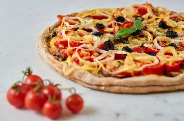 Pizza vegetariana caliente con tomates, pimiento, cebolla, aceitunas negras, queso y especias sobre fondo blanco de cerca decorado con albahaca fresca y tomates cherry — Foto de Stock