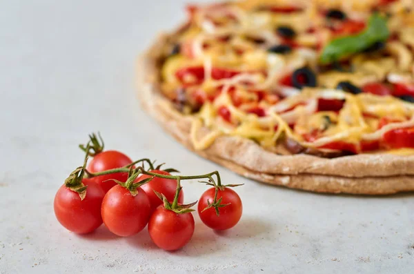 Pizza vegetariana caliente con tomates, pimiento, cebolla, aceitunas negras, queso, especias sobre fondo blanco borroso de cerca decorado con albahaca fresca y pequeños tomates cherry en primer plano — Foto de Stock