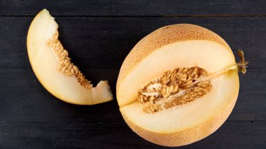 Taze tatlı sarı kavun ahşap siyah masanın üzerine dilimlenmiş. Ham organik kavun ahşap koyu arka plan bulanık üzerinde izole parçası yakın çekim