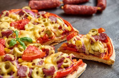 Parça pizza salam, domates, dolmalık biber, soğan, yeşil zeytin, Mısır, peynir ve baharatlar ile. Küçük sosis salam kahverengi ahşap masa üzerinde pizza ans dilimlenmiş arka plan bulanık üzerinde kapat