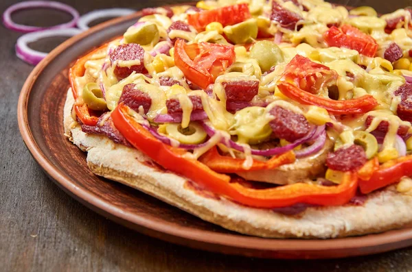 Pizza con salami, tomates, pimiento, cebolla, aceitunas verdes, maíz, queso y especias sobre fondo de madera marrón — Foto de Stock