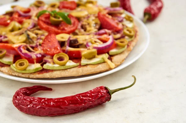 Pimienta picante roja en la superficie blanca de cerca. Sobre fondo borroso pizza vegetariana con tomates, pimiento, cebolla, aceitunas verdes, queso y especias — Foto de Stock