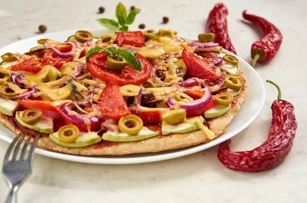 Pizza vegetariana con tomates, pimiento, aros de cebolla, aceitunas verdes, queso y especias sobre fondo blanco de cerca decorado con albahaca fresca, tres chiles y tenedor de plata — Foto de Stock