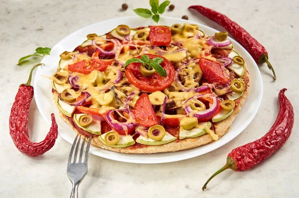 Pizza vegetariana con tomates, pimiento, aros de cebolla, aceitunas verdes, queso y especias sobre fondo blanco de cerca decorado con albahaca fresca, tres chiles y tenedor de plata — Foto de Stock