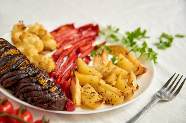 Patatas fritas, berenjena, pimiento morrón y coliflor en plato blanco de cerca decorado con tenedor, tomates cherry frescos y perejil verde — Foto de Stock