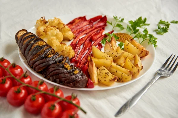 Patatas fritas, berenjena, pimiento y coliflor en plato blanco decorado con tenedor, tomates cherry frescos y perejil verde — Foto de Stock