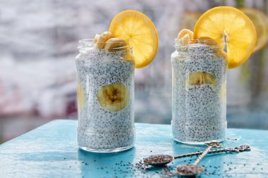 Muz puding chia ve turuncu kavanozların içinde. İki vintage kaşık mavi ahşap tahta üzerinde ham chia tohum ile süslenmiş. Sağlıklı suprefoods tatlı veya arka plan bulanık Kahvaltı