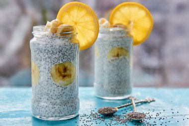 Muzlu süt puding chia ve turuncu cam ile yakın çekim iki vintage kaşık mavi ahşap tahta üzerinde ham chia tohum ile süslenmiş. Sağlıklı suprefoods tatlı ya da kahvaltı. Yan görünüm