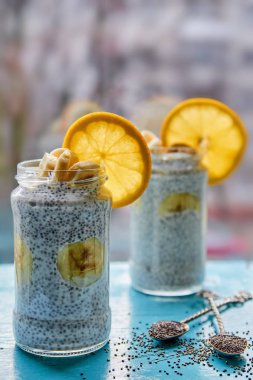 Muzlu süt pudingle chia ve turuncu iki kaşık mavi ahşap tahta üzerinde ham chia tohum ile süslenmiş kavanozların içinde. Sağlıklı suprefoods tatlı veya kahvaltı üzerinde arka plan bulanık. Yatay