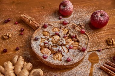 Lezzetli elmalı turta taze kızılcık ve ceviz ile elma, zencefil ve tarçın ile dekore edilmiştir. Toz elmalı turta ahşap kahverengi zemin üzerinde yemeye hazır. Yan görünüm