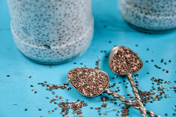 Raw fresh chia seeds in two vintage spoons on the turquoise wooden table. Detox superfoods breakfast - chia healthy smoothie pudding on the blurred  background. Close up view