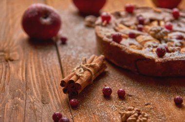 Ahşap kahverengi zemin üzerine tarçın sopa. Taze kızılcık ve elma ve tarçın bulanık arka plan üzerinde süslenmiş ceviz ile toz elmalı turta. Görünümü kapatın