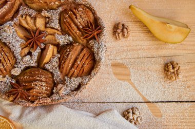 Bir parça toz armut turta beyaz bez ve kaşık, kurutulmuş portakal, ceviz ile anason yıldız dekore edilmiş ve ahşap tahta üzerinde taze armut dilimlenmiş. Ahşap arka plan üzerinde sağlıklı ev yapımı armut pasta