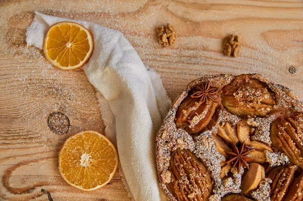 A piece of powdered pear pie decorated with white cloth, dried oranges, walnuts on the wooden board. Healthy vegetarian homemade pear pie on the wooden background. Top view