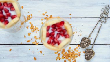 Chia tohum ve dağınık granola tahıl beyaz tahta masada iki vintage kaşıklarla. Granola puding gözlük ile taze dilimlenmiş muz ve nar tohumları üzerinde arka plan bulanık. Üstten Görünüm