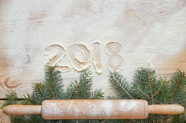 Sign happy New year 2018 in the flour on the wooden table decorated with christmas three branches and powdered rolling pin. Top view. Copy space