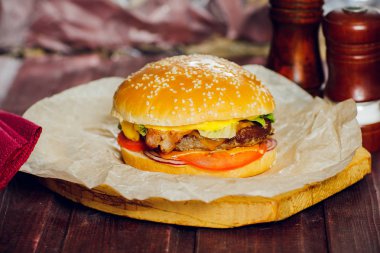 Biftekli hamburger, kızarmış pastırma, soğan, domates, marul ve ahşap zemin üzerinde salatalık ezmesi.