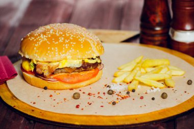 Biftekli hamburger, kızarmış pastırma, soğan, domates, marul ve ahşap zemin üzerinde salatalık ezmesi.