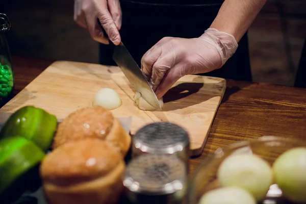 Chef\'s hands with knife cutting the onion on the wooden board. Preparation for cooking. Healthy eating and lifestyle.