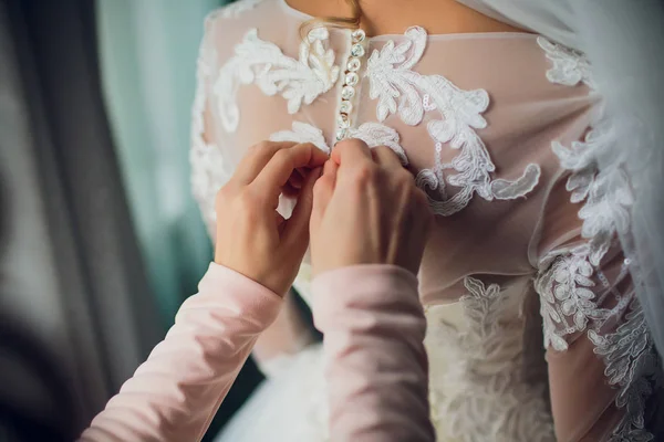 Bruidsmeisje maakt strik-knoop op de achterkant van bruiden trouwjurk — Stockfoto