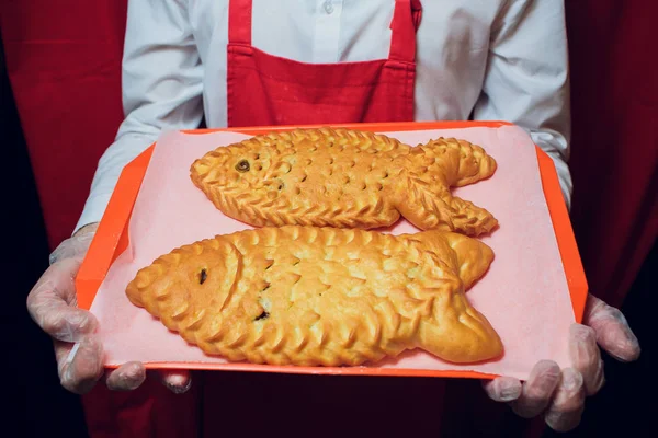 Baker mantiene una bandeja con el hombre pan fresco en panadero uniforme rojo y blanco sosteniendo una bandeja con la fabricación de pan — Foto de Stock